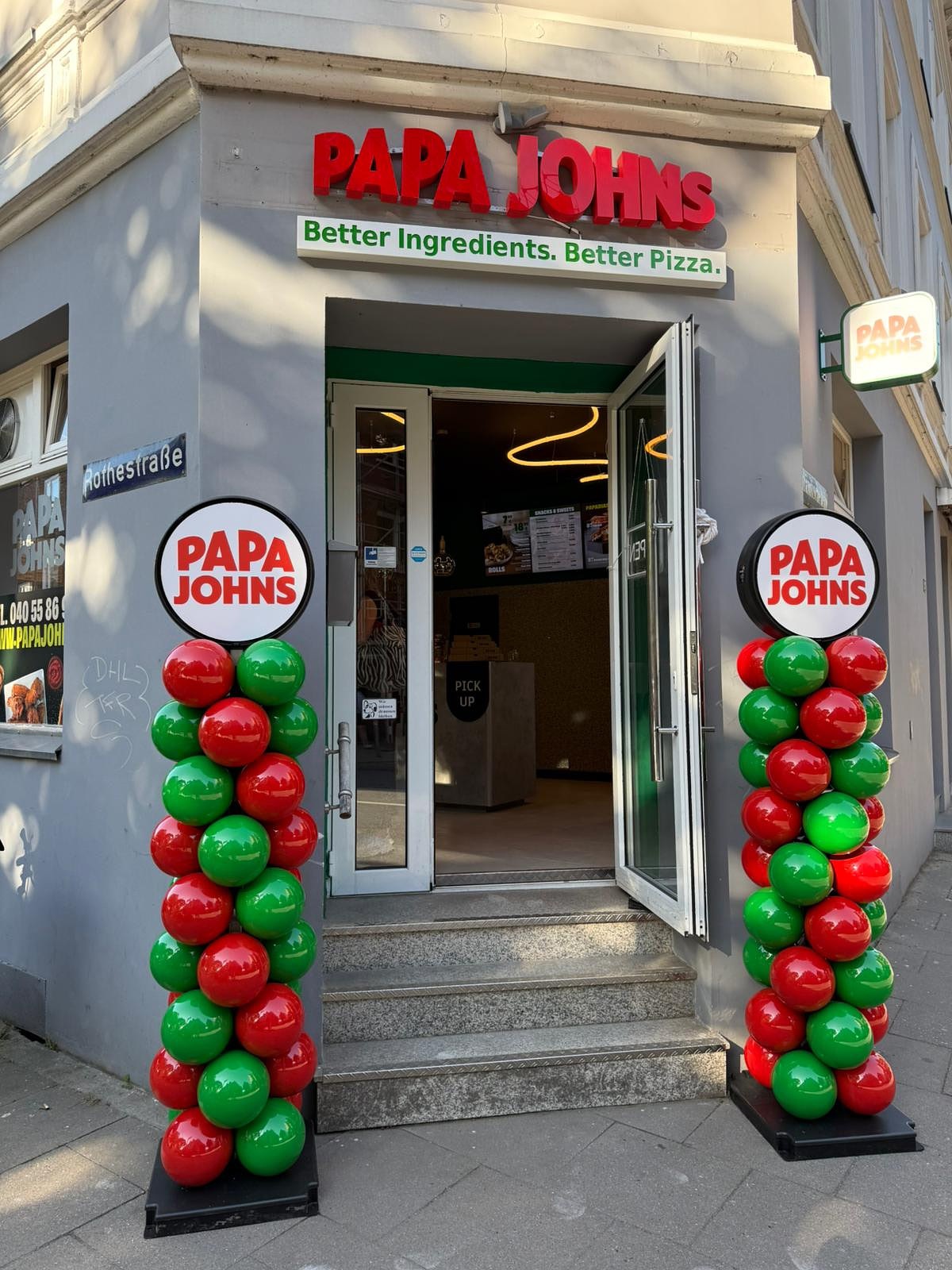 Eingang eines Papa Johns Stores mit rot-grünen Ballonsäulen